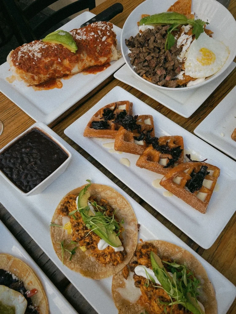 Overhead view: burritos, tacos, waffles, and chilaquiles on a table.