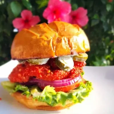 Close-up of colorful crispy sandwich with pickles, tomato, and flowers.