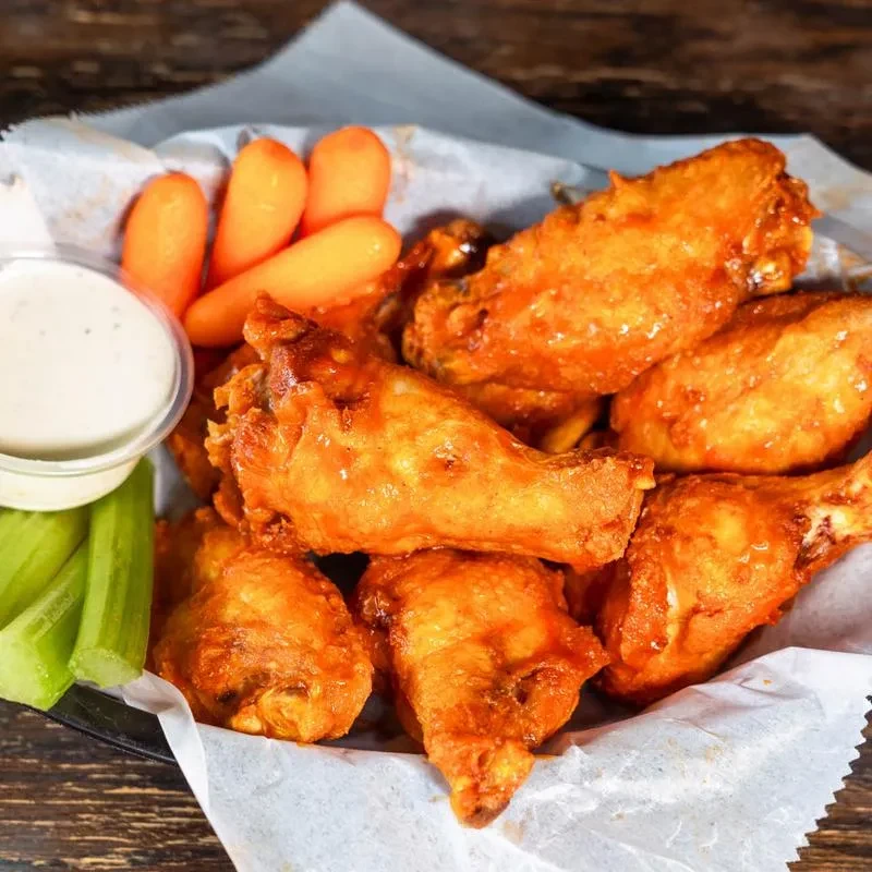 Basket of Buffalo wings, creamy dip, celery, and baby carrots.