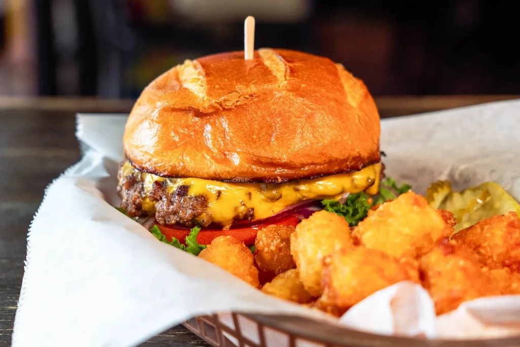 Cheeseburger with melted cheese, lettuce, tomato, tater tots, and pickles.