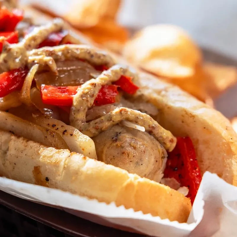 Gourmet sausage in toasted bun with onions, bell peppers, and mustard.