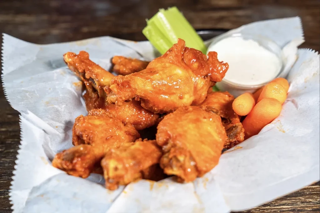 Chicken wings with orange-red sauce, celery, carrots, and white dip.