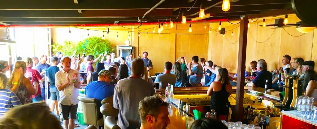 Lively, crowded bar with people socializing, drinking, and string lights.