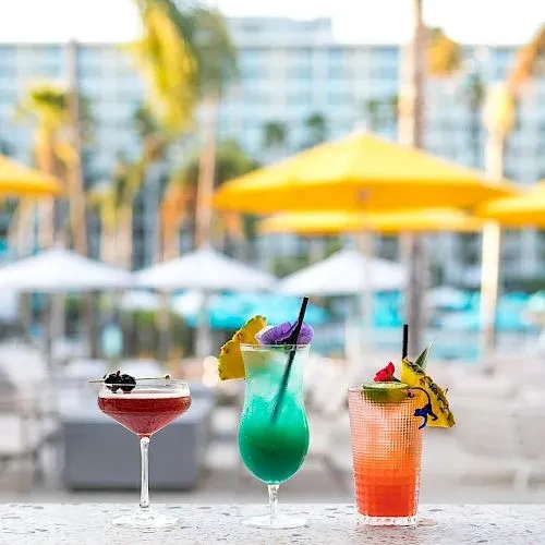 Three vibrant, garnished cocktails at a sunny outdoor resort bar.