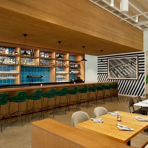 Empty modern restaurant with teal bar, green velvet stools, and wood ceiling.