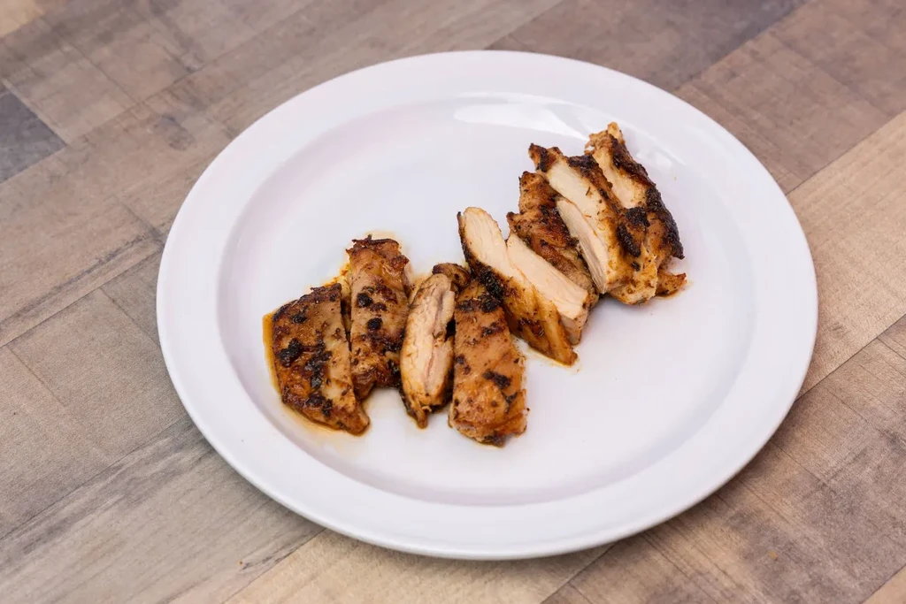Golden-brown grilled chicken slices on a white plate and wooden table.