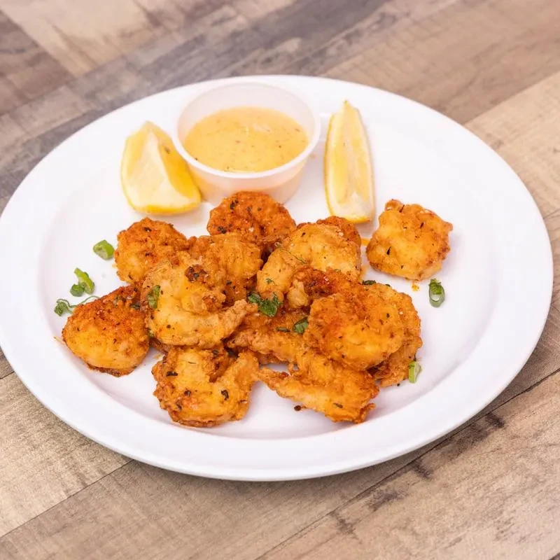 Plate of golden fried shrimp, lemon wedges, and dipping sauce on wood.