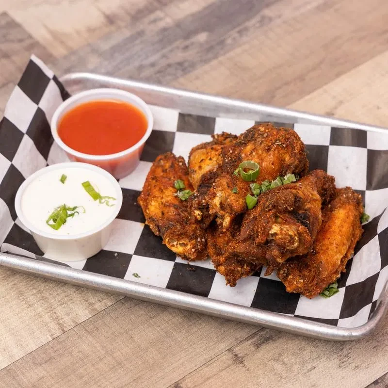 Fried chicken wings with green onions, two sauces on a checkered tray.