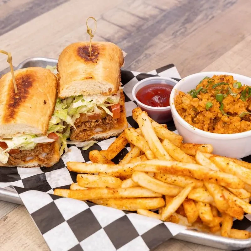 Po'boy sandwich, seasoned fries, ketchup, and spiced rice on a tray.