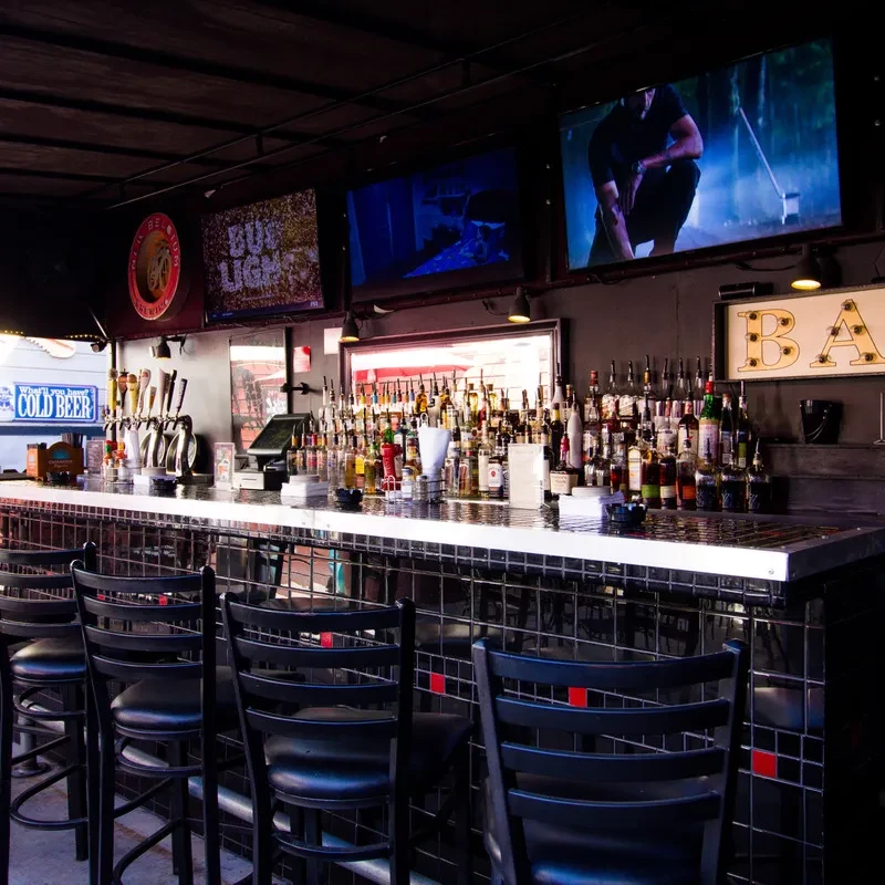 Modern, well-stocked bar with liquor, beer taps, TVs, and empty barstools.