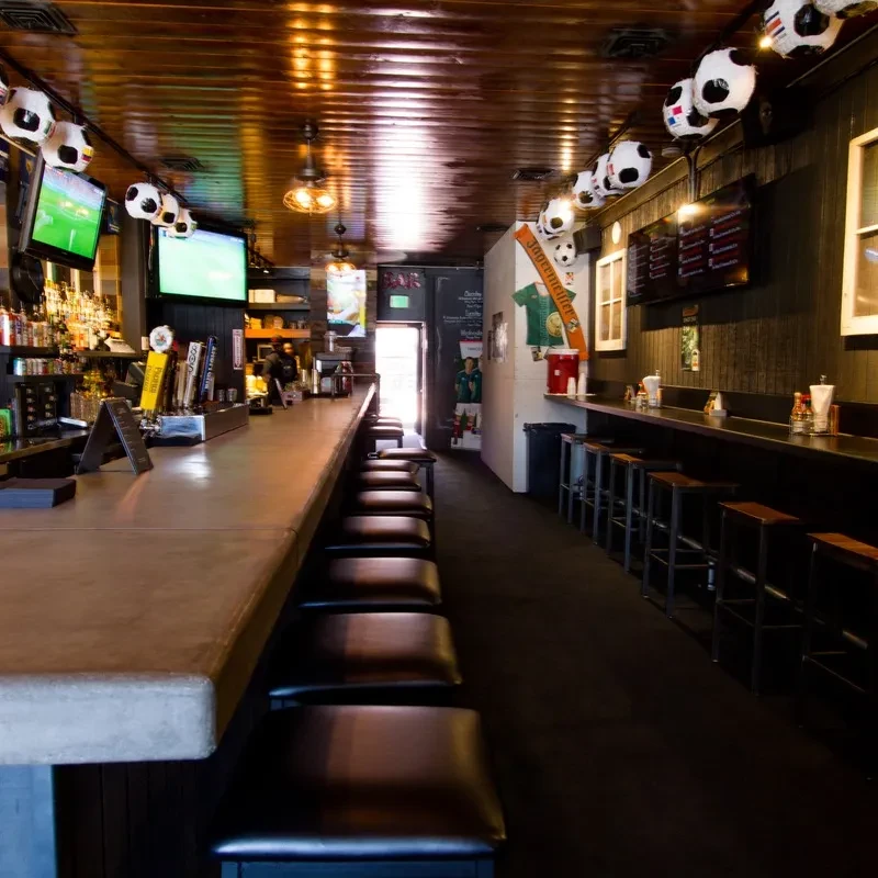 Casual sports bar interior with a long bar, taps, TVs, and soccer decor.