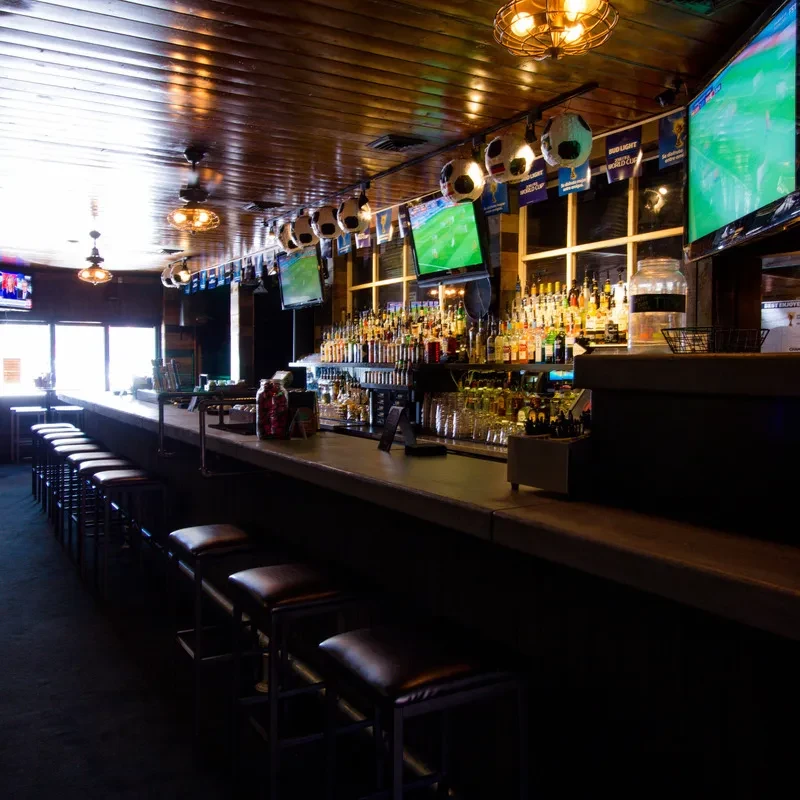 A well-stocked sports bar interior featuring multiple TVs and soccer decor.