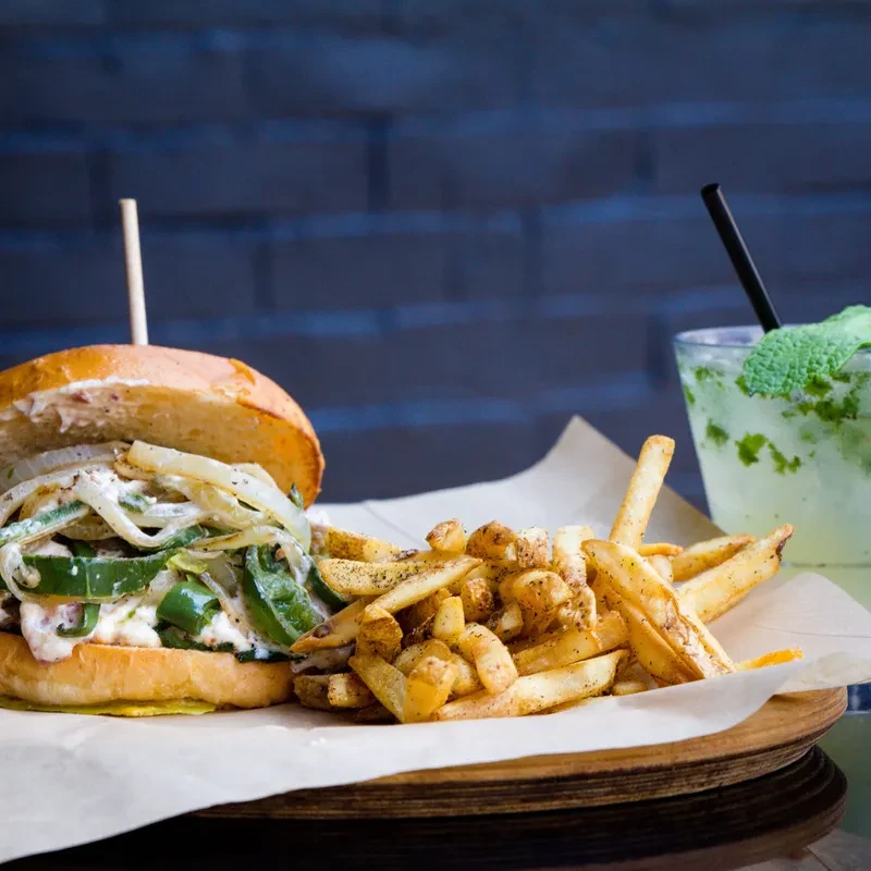 Close-up of burger, seasoned fries, and mint drink on wooden board.