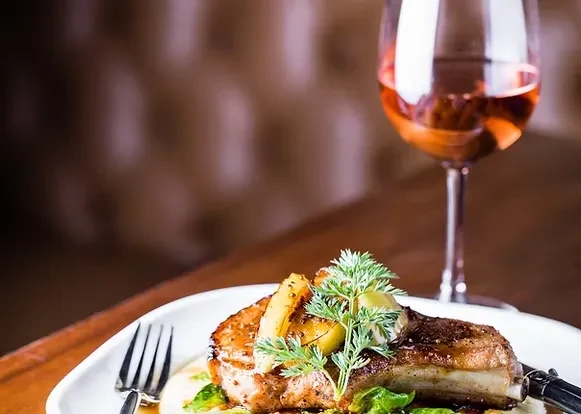 Perfectly plated pork chop with roasted vegetables, sauce, herbs, and wine.