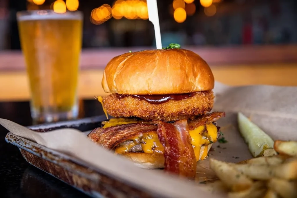 Gourmet burger with double patty, bacon, fried onion ring, fries, beer.