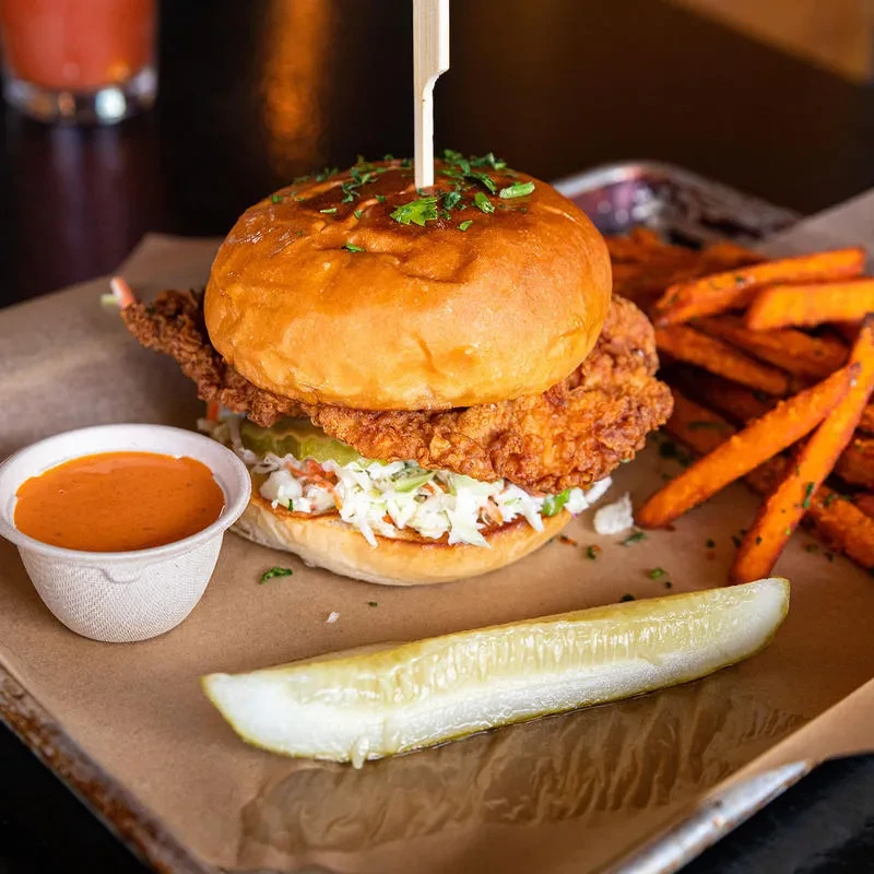 Fried chicken sandwich with coleslaw, sweet potato fries, sauce, and pickle.