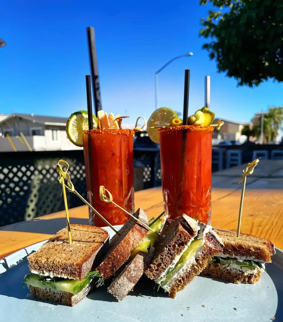 Outdoor table with cucumber sandwiches and two garnished Bloody Marys.