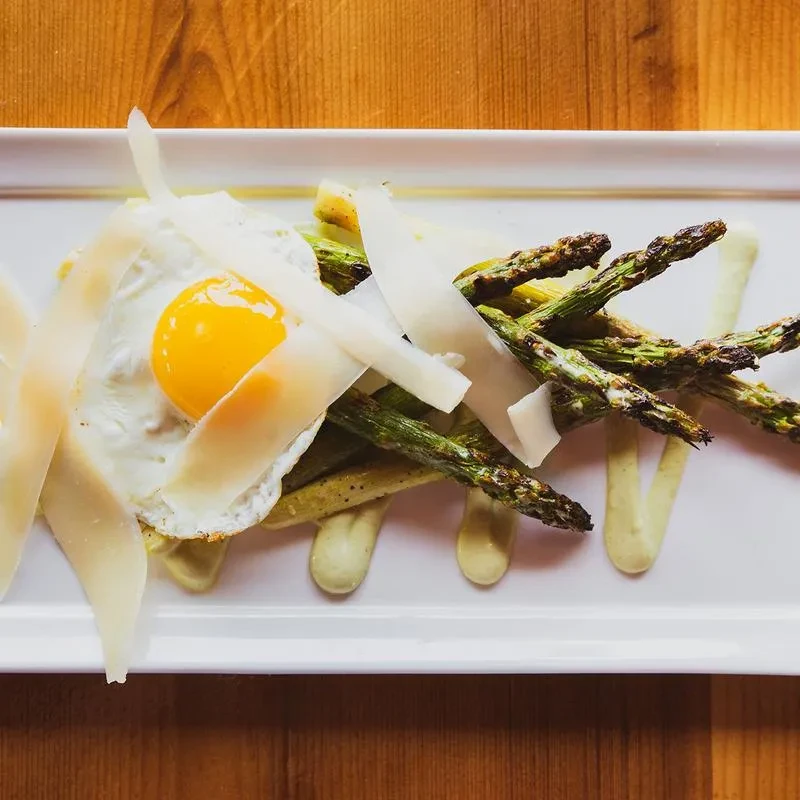 Roasted asparagus, fried egg, cheese, and green sauce on a plate.