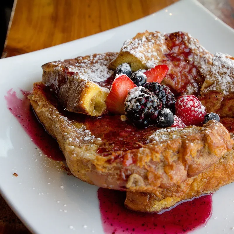 Golden-brown French toast with berry compote, fresh berries, and powdered sugar.