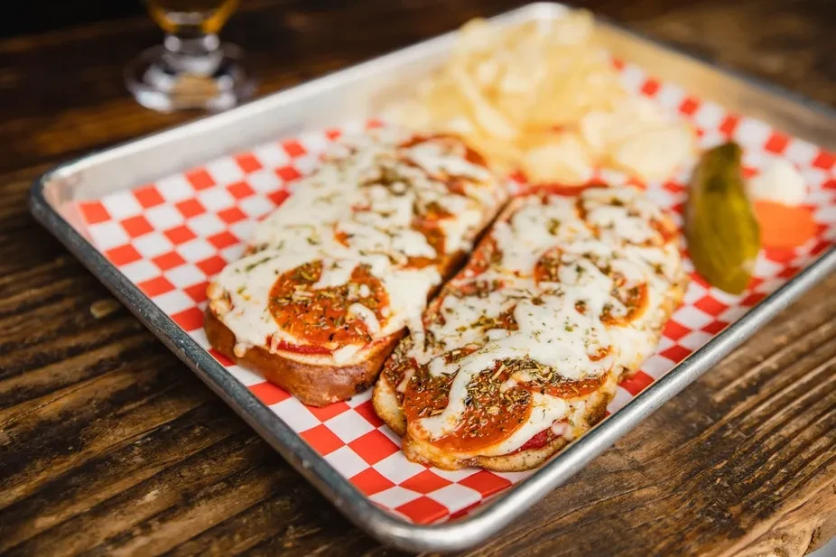 Two pepperoni mini pizzas with chips and a pickle spear.