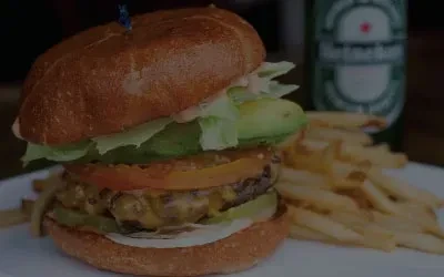 Stacked cheeseburger, fries, and Heineken bottle on a white plate.