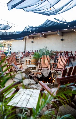 Rustic patio with stone fire pit, Adirondack chairs, and strung lights.