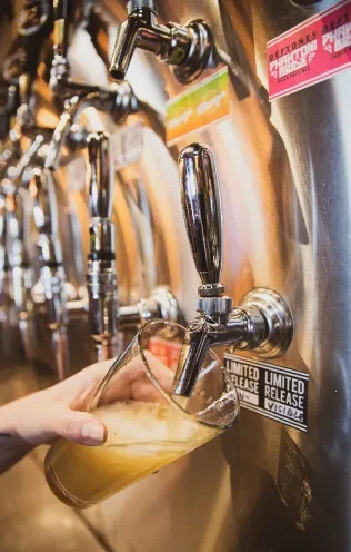 Hand pours frothy beer from stainless tap labeled "Deftones IPA".