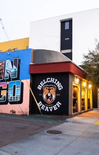 Exterior of Belching Beaver Brewery sign and San Diego mural at dusk.
