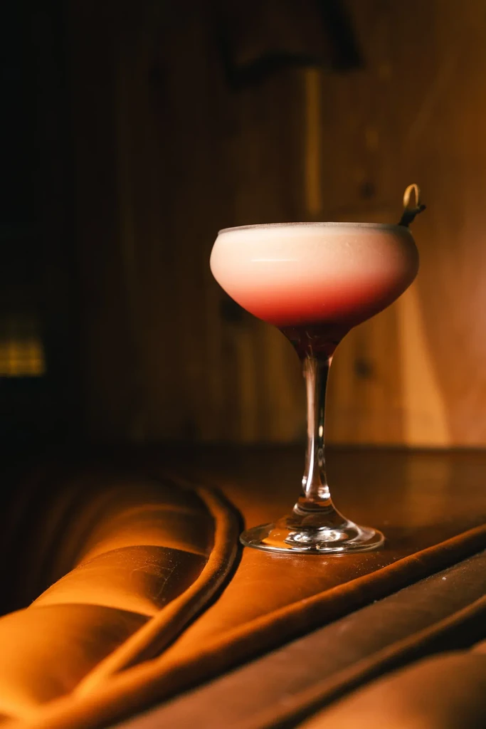 Gradient pink and red cocktail in a coupe glass with twisted garnish.