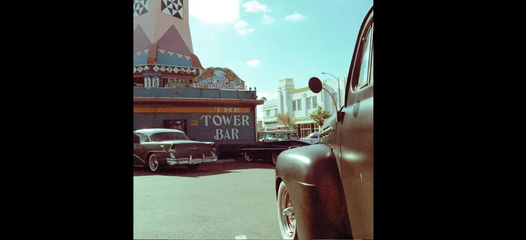 Vintage street scene featuring Tower Bar building and classic cars.