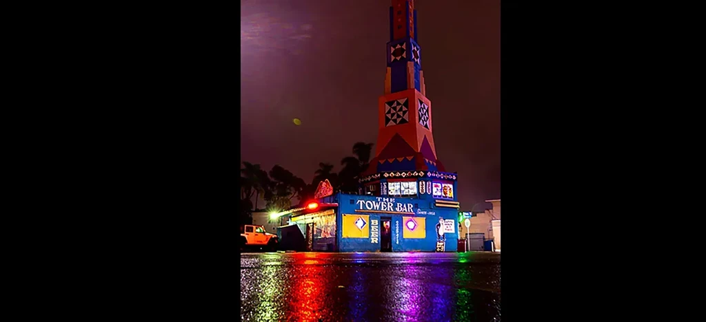 Colorful abstract tower, "THE TOWER BAR" building, reflected on wet ground.