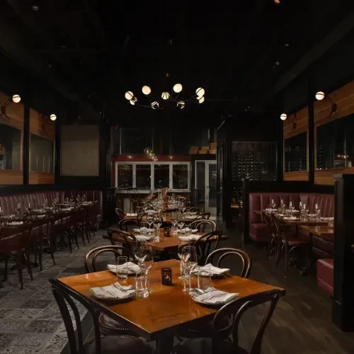 Dimly lit, empty restaurant interior with red booths and set wooden tables.