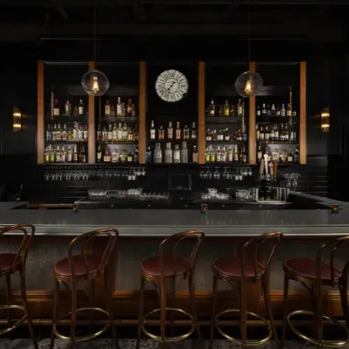 Elegant dark bar with well-stocked liquor shelves and empty stools.