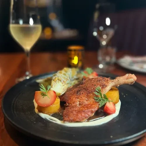 Crispy poultry leg, roasted potatoes, vegetable, white sauce, and red fruit.