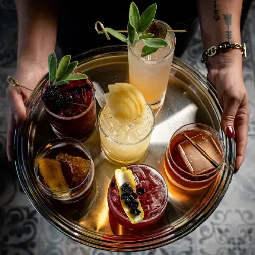 Overhead: Hands holding a silver tray with six distinct cocktails.