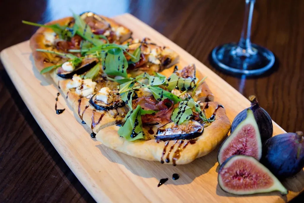 Flatbread topped with figs, prosciutto, goat cheese, arugula, and balsamic glaze.
