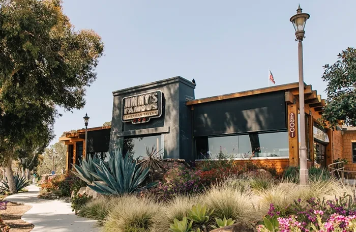 Sunny exterior of modern Jimmy's Tavern, dark grey and wood building.