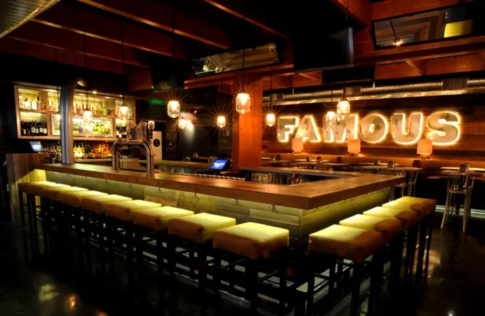 Empty, modern bar with glowing counter, stocked shelves, and "FAMOUS" sign.
