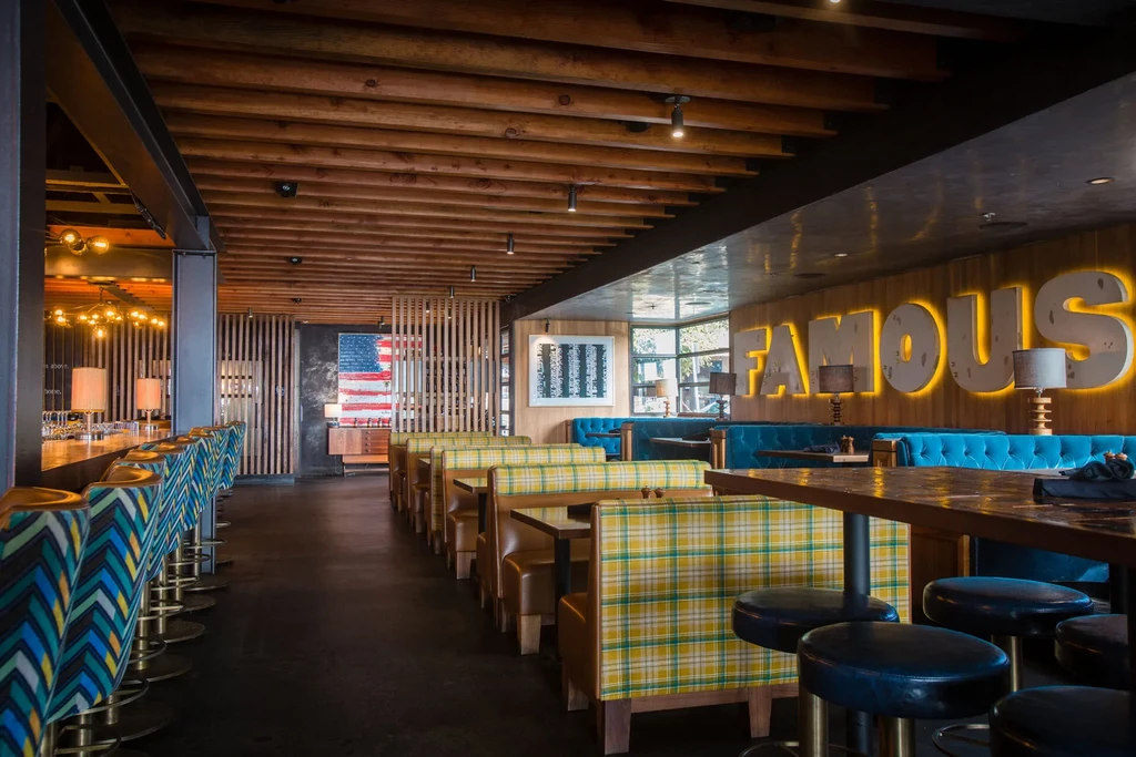 Modern, eclectic restaurant interior with diverse seating, a bar, and wooden beams.