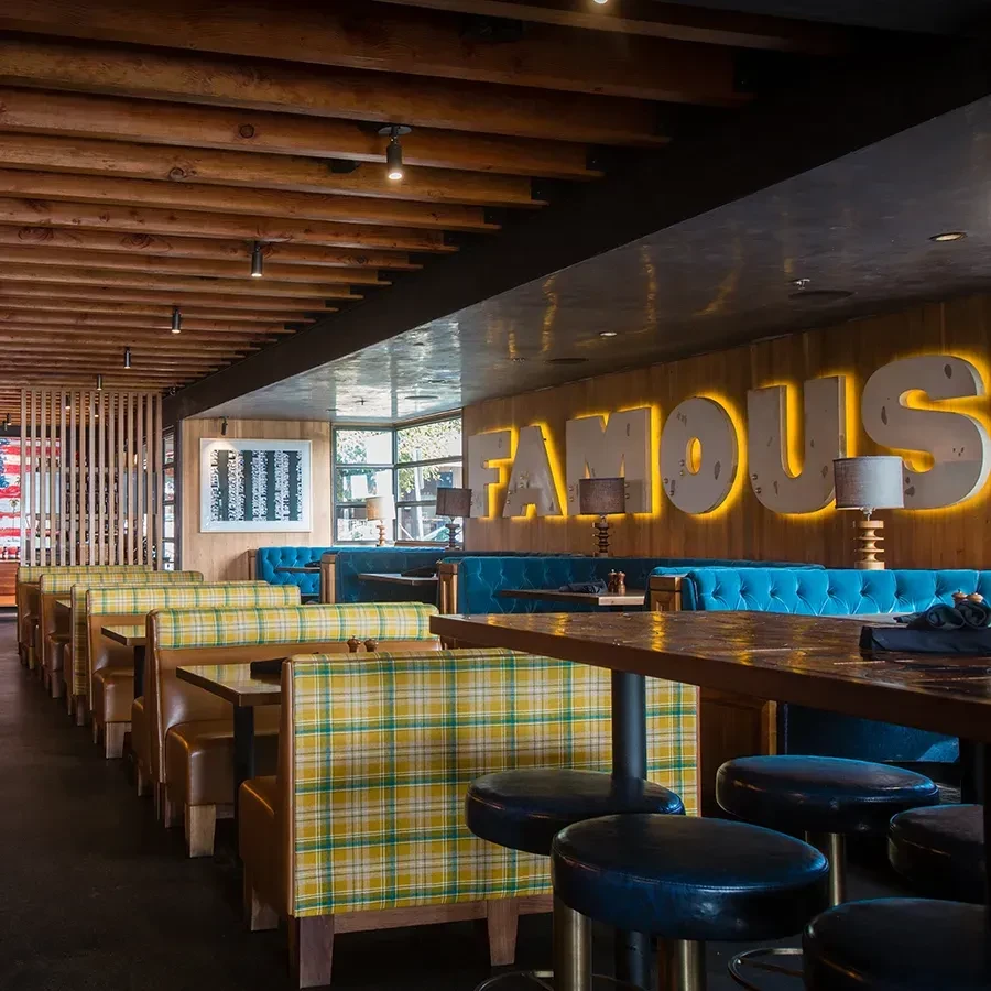 Modern restaurant interior with plaid booths, blue banquettes, and 'FAMOUS' sign.