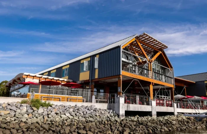 Modern multi-level building with wood beams, red umbrellas, by water.