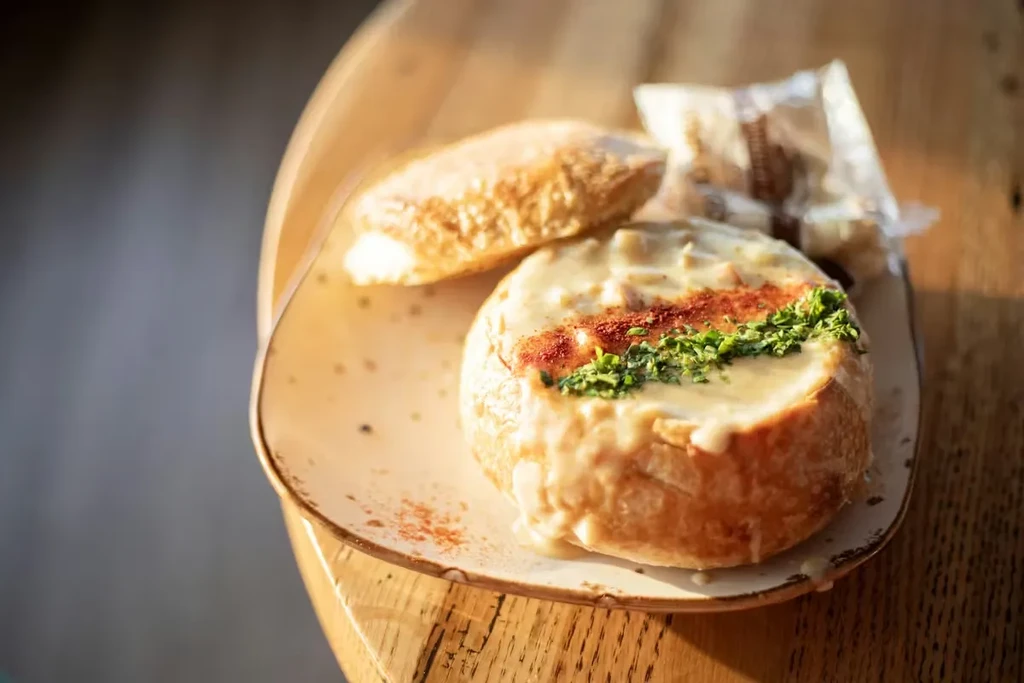 Creamy soup in a golden-brown bread bowl with herbs, crackers.