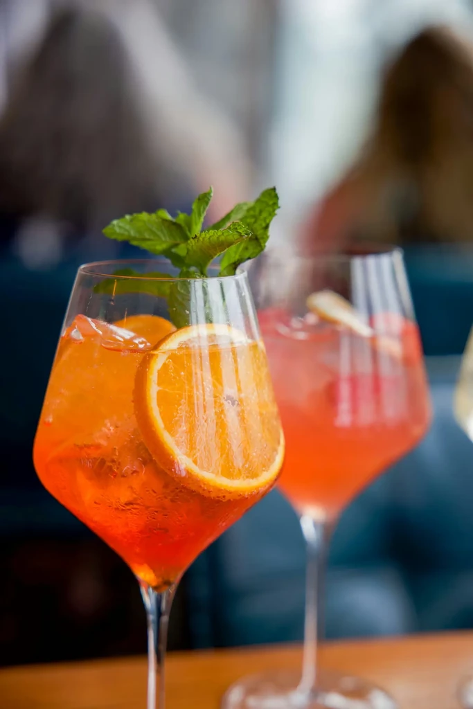Two brightly colored cocktails in stemmed glasses with fruit garnishes.