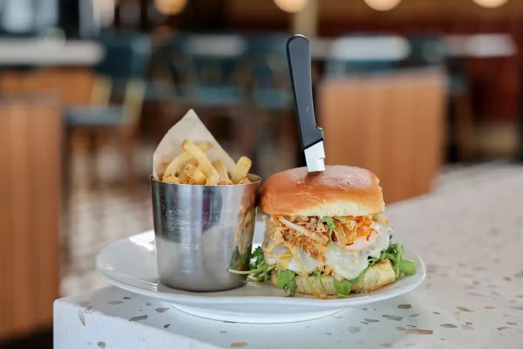 Gourmet burger with fried egg and french fries in a metal cup.