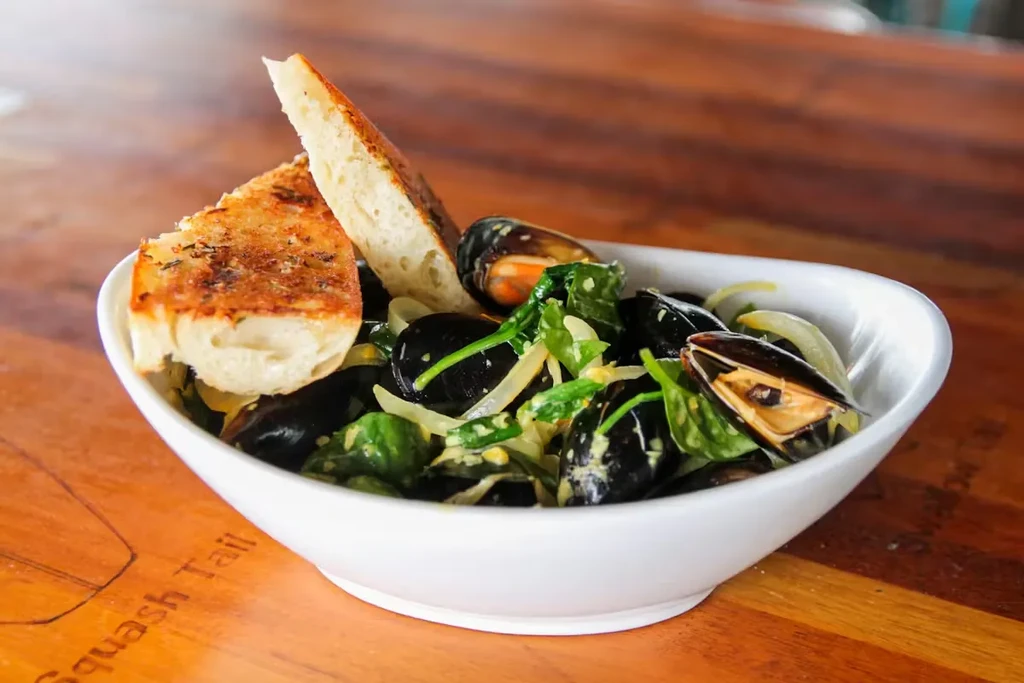 Steamed mussels in creamy sauce with greens and toasted bread.