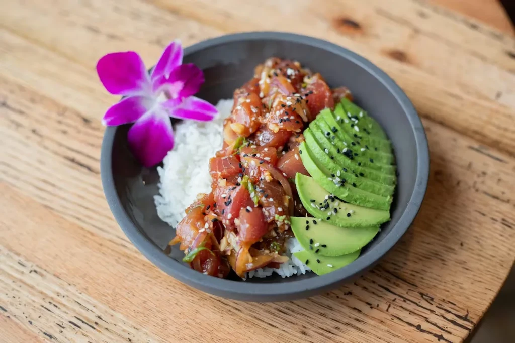 Colorful poke bowl with tuna, rice, avocado, and a purple orchid.