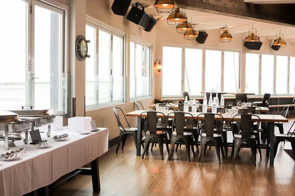 Industrial-style restaurant with buffet, dining tables, and bright waterfront windows.