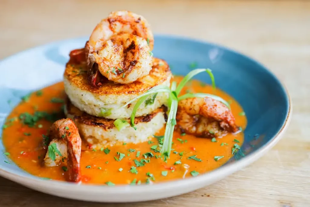 Shrimp and stacked golden patties in orange sauce, garnished with herbs.