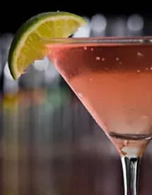 Pinkish-red cocktail in a martini glass with a lime wedge.