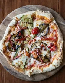 Rustic pizza with grilled zucchini, eggplant, tomatoes on a wooden board.